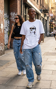 Two people walking down a street with graffiti on the wall.