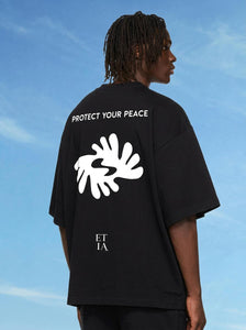 Person wearing a black t-shirt with 'Protect Your Peace' text and white graphic design against a blue sky.